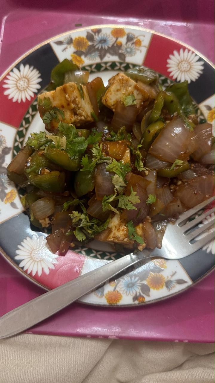 Chilli paneer tossed with green capsicum and onion on a floral plate, garnished with coriander