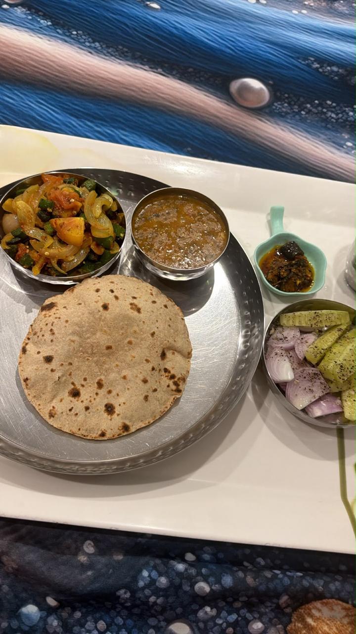 A steel thali with a puffed roti, a bowl of bhindi masala, a bowl of dal, kachumber and a small dish of achaar