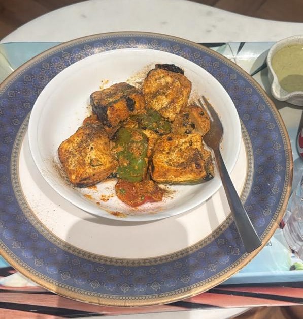 A white bowl of char-grilled paneer tikka with capsicum on a blue-rimmed plate