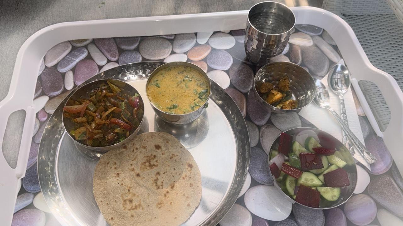 A thali on a pebble-print tray with a roti, mixed vegetable stir-fry, dal, a salad and a steel glass