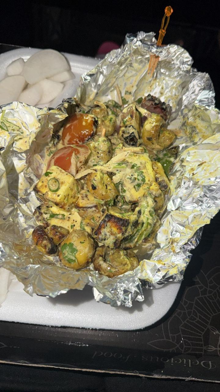 Malai paneer and mushroom tikka served in foil inside a takeaway container, with sliced radish on the side
