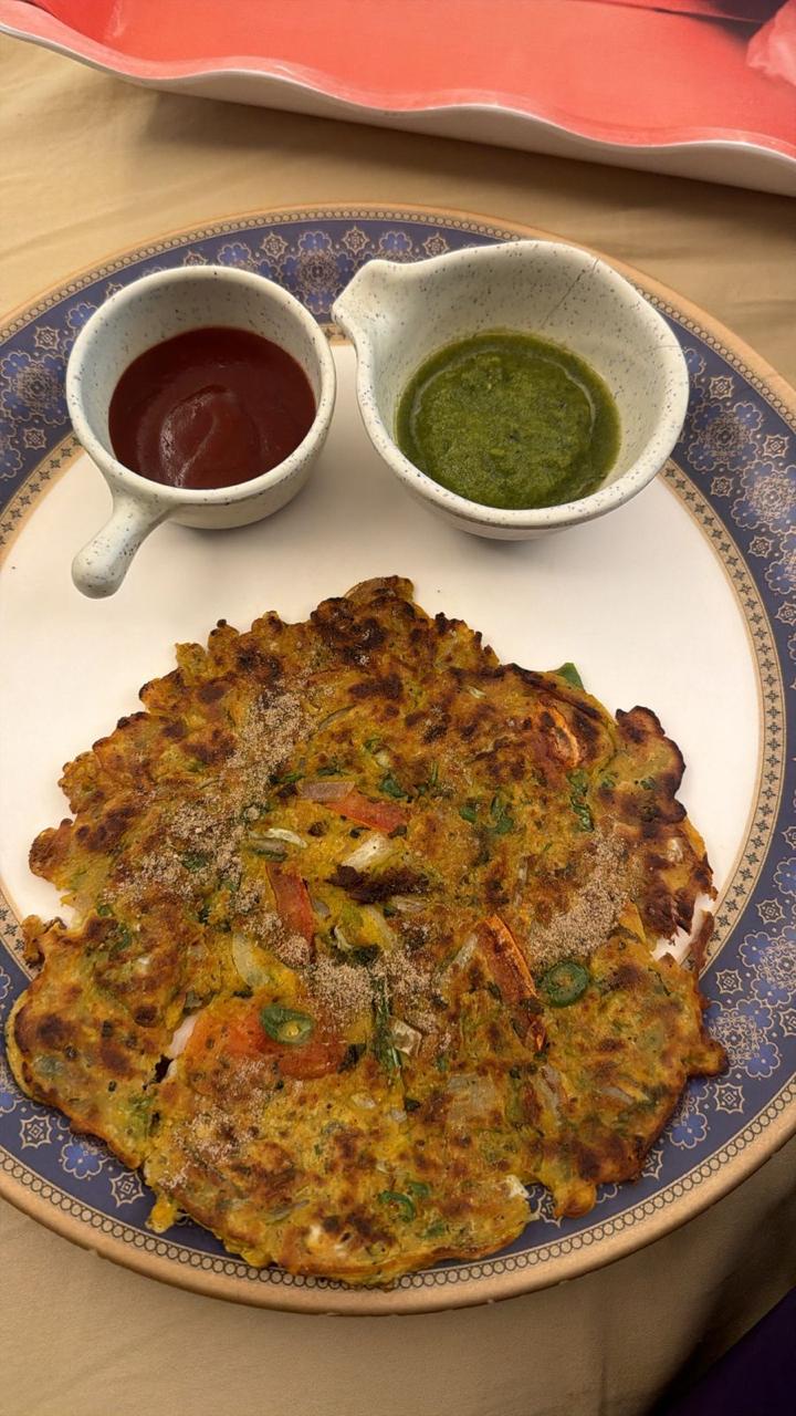 A golden moong dal cheela on a blue-rimmed plate with green chutney and ketchup in small cups