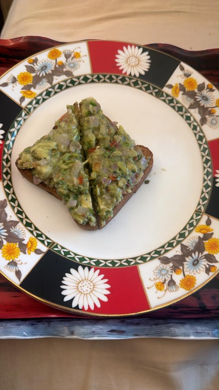 Avocado toast cut into two halves on an ornate floral plate with a gold rim