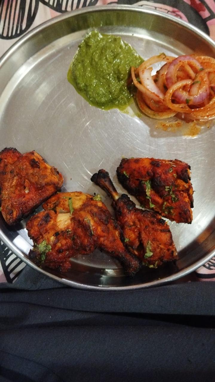A steel plate of tandoori chicken pieces with green chutney and marinated onion rings