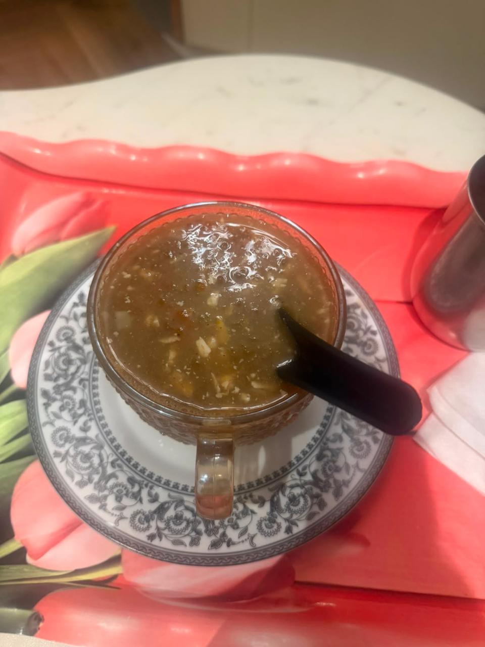 A glass cup of thick vegetable soup on a patterned saucer, with a spoon and napkins beside it